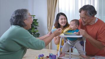 un pequeño niño comiendo su primero comida, padres y abuelos animar emocionado foto