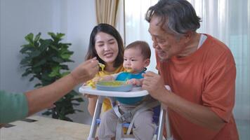 un pequeño niño comiendo su primero comida, padres y abuelos animar emocionado foto