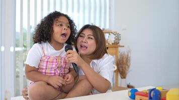 A tiny girl and mother sits on a toy table, clutching a microphone, and sings cheerfully in the living room photo
