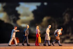 Miniature figures carrying luggage walk against a somber backdrop, symbolizing displacement and the human cost of war photo