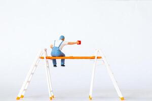 Miniature figure of a painter sitting on ladders holding a red paint can on white background photo