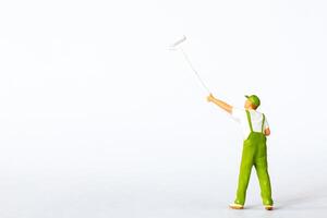 A miniature figure of a painter using a long roller brush to paint on a white background photo