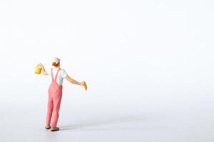 Miniature figure dressed in pink overalls and a white cap on a clean white background photo