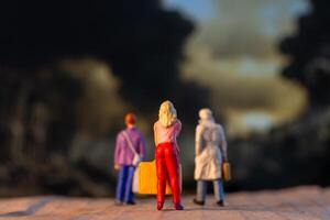 Miniature figures carrying luggage walk against a somber backdrop, symbolizing displacement and the human cost of war photo