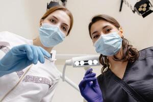 From below female dentists with mirror and device bending over patient during appointment in dental clinic photo