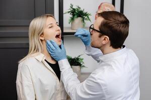 Doctor using inspection spatula to examine patient throat. ENT doctor doing throat exam of a woman. Patient opened her mouth to throat check-up photo