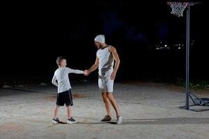 A young man and a boy shake hands before playing basketball in the evening in the park photo