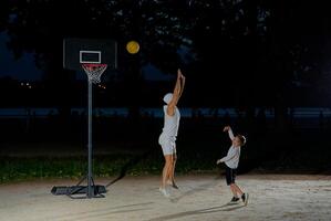 A father and son enjoy a night basketball game at a local park under bright lights focusing on teamwork and fun photo