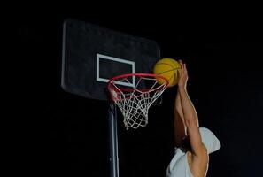 A man performs a slam dunk on a basketball court at night under the glare of bright outdoor lights photo