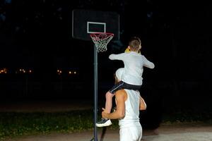 A father and son share a fun moment playing basketball outdoors at night with a hoop in the background photo