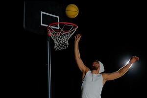 A man performs a slam dunk on a basketball court at night under the glare of bright outdoor lights photo