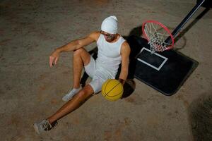 A basketball player sits on the court wearing sunglasses, relaxed after an intense practice session at dusk photo