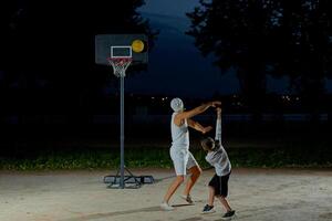 A father and son enjoy a night basketball game at a local park under bright lights focusing on teamwork and fun photo