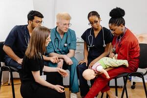 Group of doctors sitting together with baby mannequin at first aid training course photo