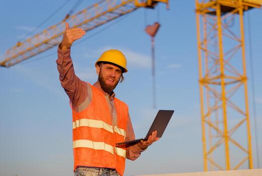 Construction engineer using laptop at building site with crane in background photo