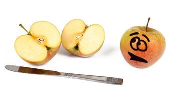 A knife and an apple with a face drawn on it photo