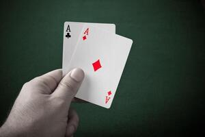 A hand holding two aces on a green table photo