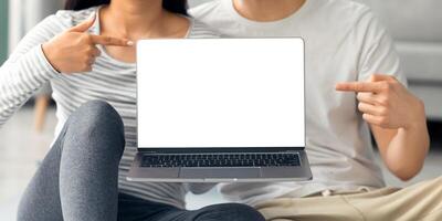 Cropped of sporty asian couple sitting on fitness mat at home and showing laptop with blank screen, young man and woman in sportswear pointing at computer with empty screen, mockup, copy space photo