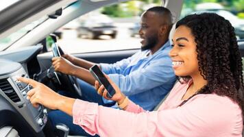 Road Trip Concept. Profile side view portrait of smiling black couple sitting in luxury car, man driving auto, woman with mobile phone pointing at the road, showing way, using digital map application photo