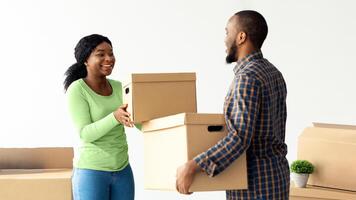 Relocation Day. Portrait Of Happy African American Couple Carrying Cardboard Boxes, Cheerful Black Spouses Moving To New Apartment, Packing Belongings And Smiling To Each Otrher, Free Space photo