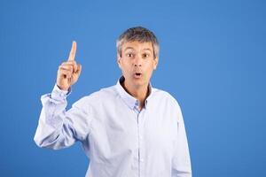 A middle aged European man with grey hair gestures with one finger raised, conveying an unexpected idea or discovery. He appears animated and engaged in conversation. photo