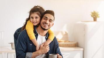 Time With Daddy. Portrait Of Happy Arab Father And Little Daughter Embracing While Having Snacks In Kitchen, Positive Middle Eastern Family Of Two Dad And Female Child Smiling At Camera, Copy Space photo