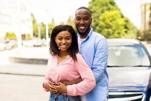 Buying New Car. Portrait Of Happy Black Couple Standing Near Their Her Automobile, Man Embracing His Wife, Puchasing Auto In Dealership Service Showroom, Smiling And Looking At Camera Outdoors photo