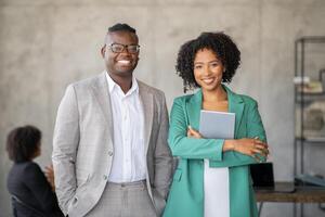 A diverse group of professionals engages in teamwork within a contemporary office environment. Two smiling leaders stand confidently in the foreground, promoting cooperation and success. photo