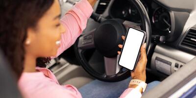 Over the shoulder view of happy black female driver holding smartphone with white blank screen, using mobile app for navigation, mock up. Closeup of cell phone with empty display, copy space template photo