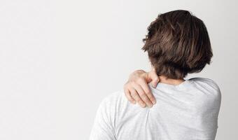 Pain in back and shoulder from working at computer. Man presses his hand to sore spot, isolated on gray background, studio shot photo