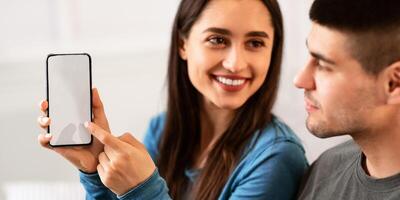 New Mobile App. Cheerful girl holding and pointing at smartphone with black screen for mockup, copy space photo