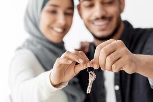 Closeup of key chain in smiling muslim couple hands, selective focus. Happy middle-eastern family husband and wife showing key from their apartment, celebrating moving to new house photo