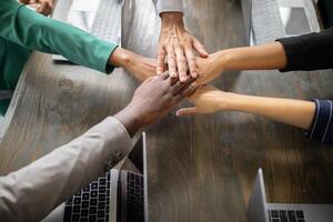 Diverse team members gather around a table in a corporate office, joining hands in a show of cooperation and commitment to success during a productive business meeting. photo