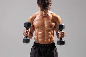 A young athletic man stands isolated in a gym environment, lifting dumbbells to enhance his strength. His dedication to fitness showcases a commitment to a healthy lifestyle. photo