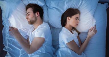 Marital Crisis, Indifference. Couple Using Cellphones Lying Back-To-Back In Bed Indifferent To Each Other. Millennial Spouses Ignoring One Another Texting With Lovers At Home. View From Above photo