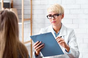Consultation in doctor office. Woman with tablet in hands listens carefully to patient in interior of office photo