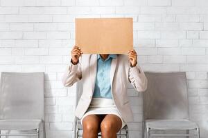 African American woman in business wear hiding behind sign with inscription I NEED WORK while waiting for work interview at office photo