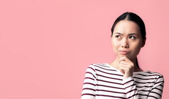 Portrait Of Pensive Korean Female Touching Chin And Looking Away With Doubt, Thoughtful Young Asian Woman Considering Interesting Offer While Standing Isolated Over Pink Background, Copy Space photo