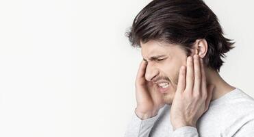 Man with earache is holding sore spot, profile on light background photo
