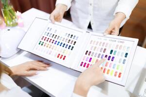 Two women enjoy a pampering experience in a salon. One points at a color chart while choosing nail polish shades, highlighting hands and fashion creativity. photo