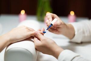 Two women are engaged in a pampering session at a salon. One is painting the others nails with vibrant blue polish, creating a fashionable look while candles provide a relaxing ambiance. photo