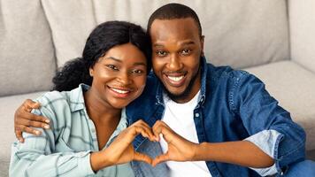 Portrait Of Joyful Romantic African American Couple Making Heart Gesture At Camera, Smiling Black Spouses Connecting Their Hands Together Into Love Sign While Relaxing At Home, Closeup Shot photo