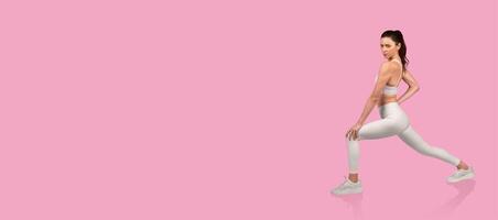 A woman is demonstrating a lunge exercise on a vibrant pink backdrop, showcasing strength and flexibility. She wears workout clothes and maintains proper form during the session. photo