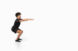 A young Brazilian man performs a squat in an isolated gym environment, showcasing athleticism and commitment to a healthy lifestyle. His focus reflects a passion for fitness, copy space photo