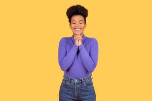 A young Hispanic woman with a joyful expression stands in front of a bright yellow background. She wears a purple top and denim jeans, embodying a cheerful lifestyle in an isolated setting. photo