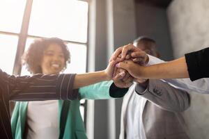 A diverse group of professionals at a corporate office collaborates enthusiastically, showcasing teamwork and unity. Their hands join in a celebratory gesture, highlighting a successful meeting. photo