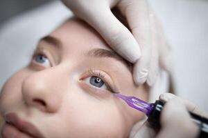 A beauty salon professional performs a permanent makeup procedure on a client. The focus is on creating a perfect eyeliner look. The environment is calm and relaxing. photo