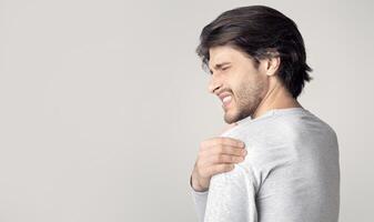 Man with painful expression, rubs shoulder with his hand, empty space photo
