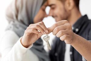 Closeup of key chain in loving muslim couple hands, selective focus. Happy middle-eastern family husband and wife showing key from their apartment, celebrating moving to new house photo