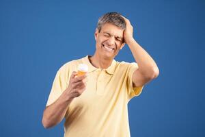 A middle aged man appears to be in discomfort while holding a bottle of medication, displaying a distressed expression. photo